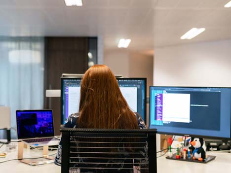 一位女子坐在辦公室內，眼前有三個螢幕正在進行 AI 學習訓練