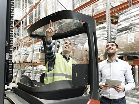 Two men in the high-bay warehouse with forklift and laptop