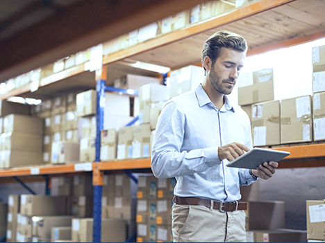 A man in a warehouse checks warehouse processes on a tablet