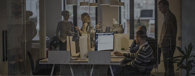 Mitarbeiter und Arbeitsplätze mit Computer hinter einer Glasfront in einem Büro